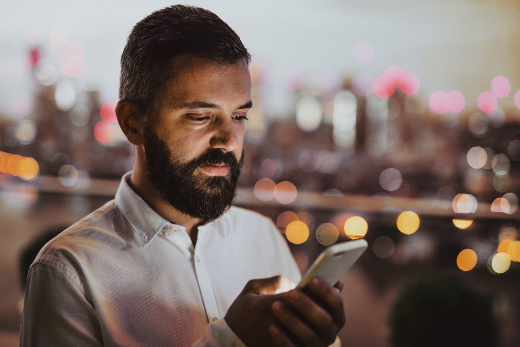 A businessman with smartphone at sunset, text messaging.